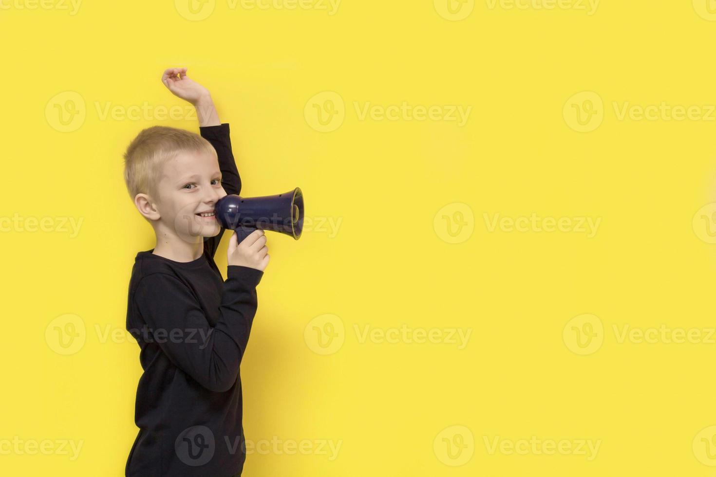 boy with a raised hand with a smile shouts into a bullhorn on a yellow background with copy space photo