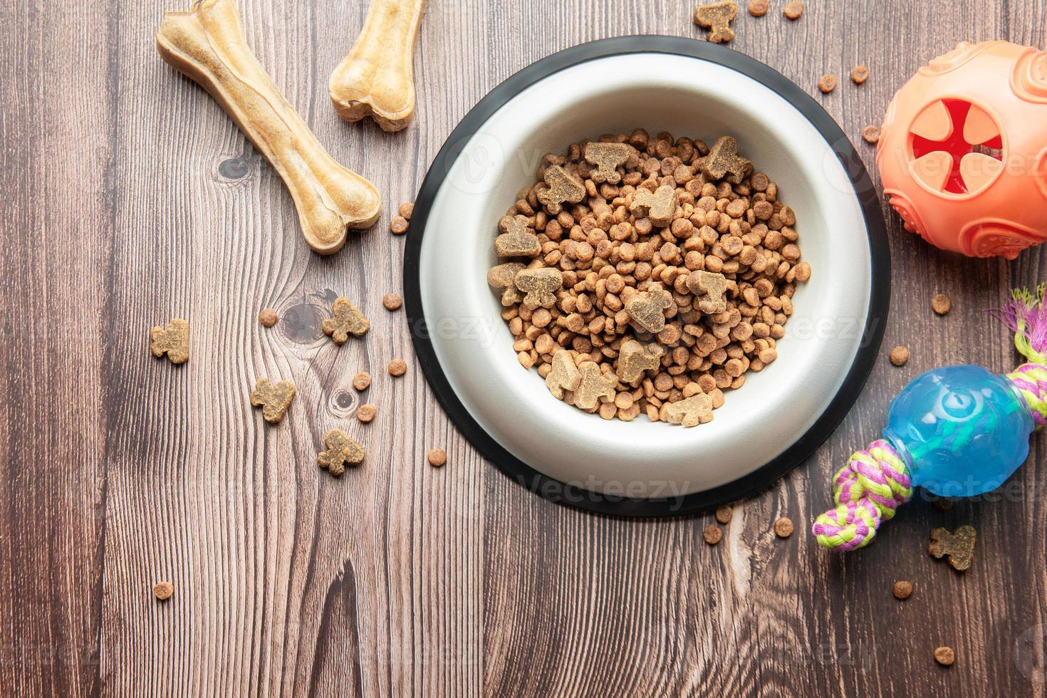 A bowl with dog food, dog treats and toys on a wooden floor. photo