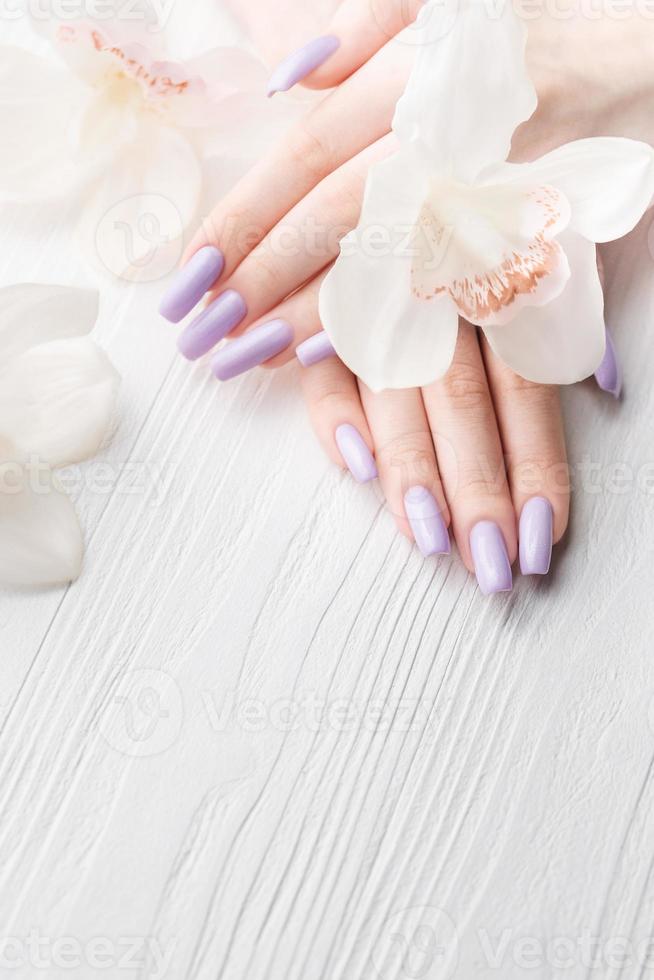 manos de niña con delicada manicura púrpura y flores de orquídeas foto