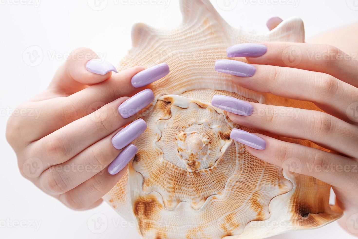 mano con largas uñas violetas cuidadas y conchas marinas foto