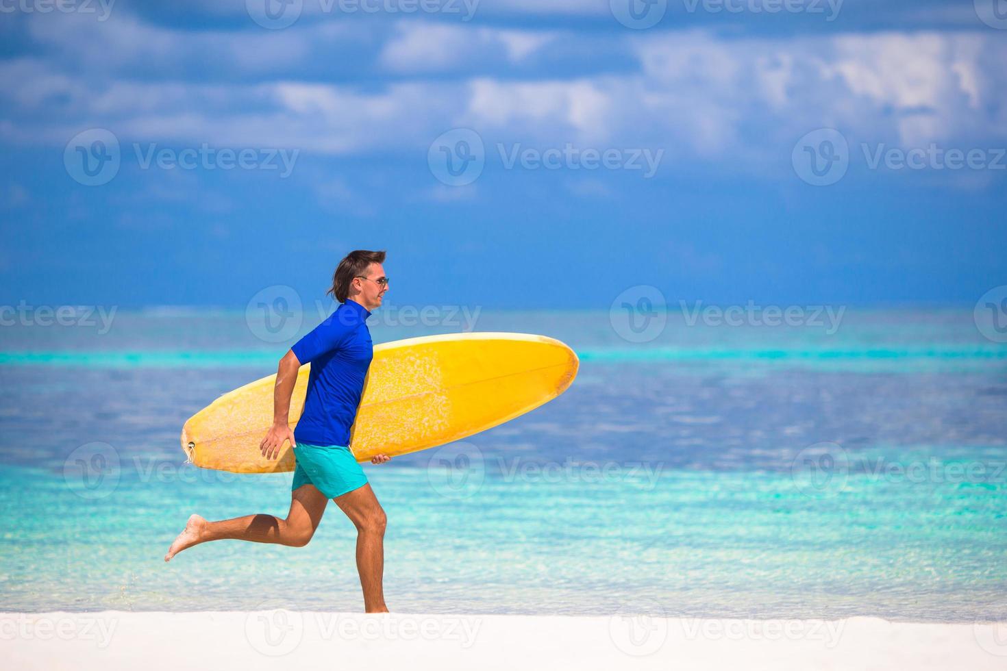 Happy young surf man runing at the beach with a surfboard photo