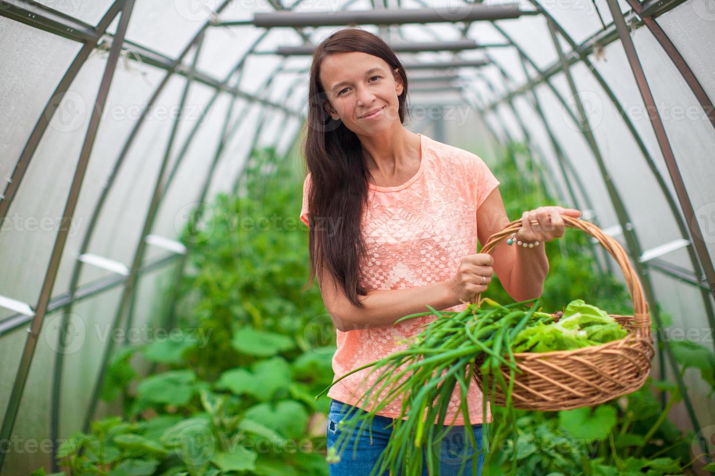 Young woman holding a basket of greenery and onion in the greenhouse photo