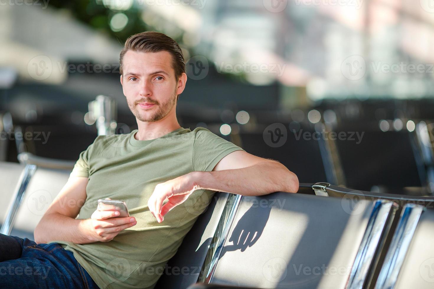 Passenger in a airport lounge waiting for flight aircraft. Young man with cellphone in airport waiting for landing photo