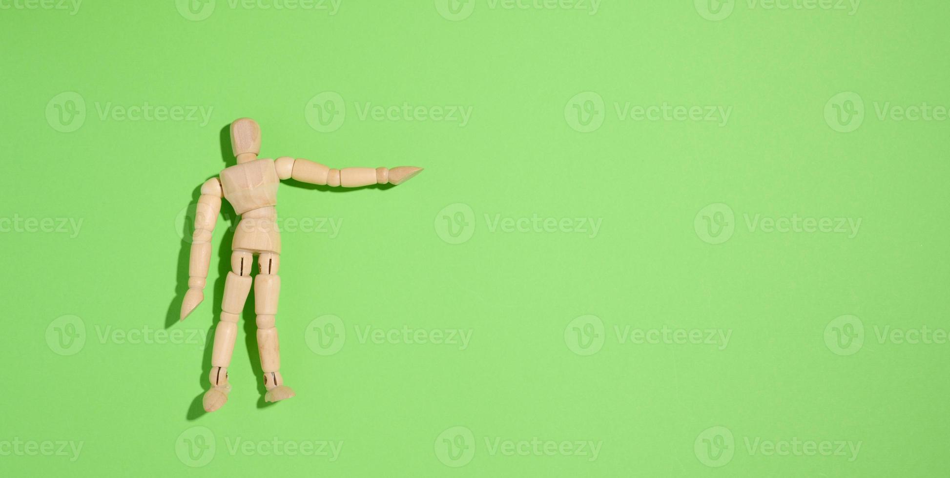 Wooden puppet man on a green background, pointing with his hand photo