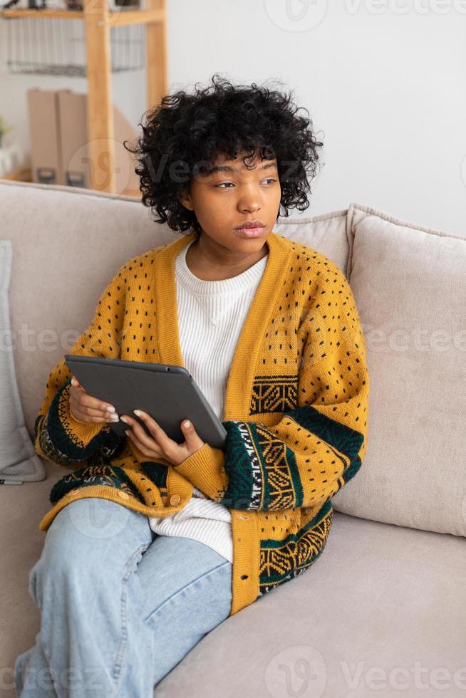 African american girl holding digital tablet touch screen typing scroll page at home. Woman with mobile tech device surfing internet using social media apps playing game. Study work shopping online. photo