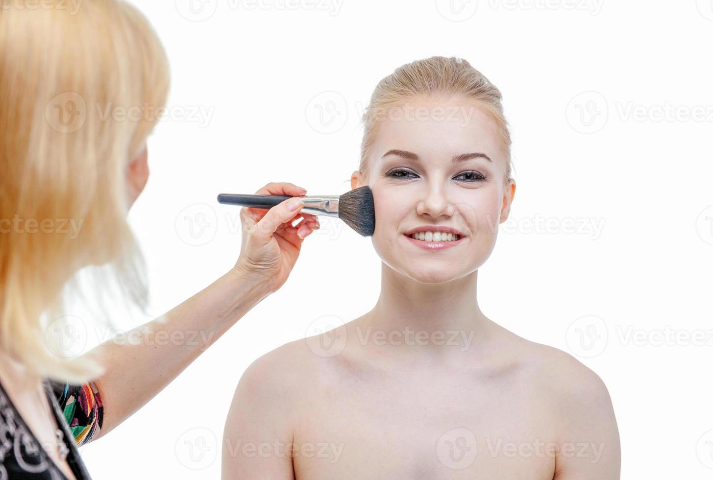 Hand of makeup master applying powder for young woman model on white background. Professional make up applying by artist. Beautiful girl face with perfect skin. Make-up detail in process. photo