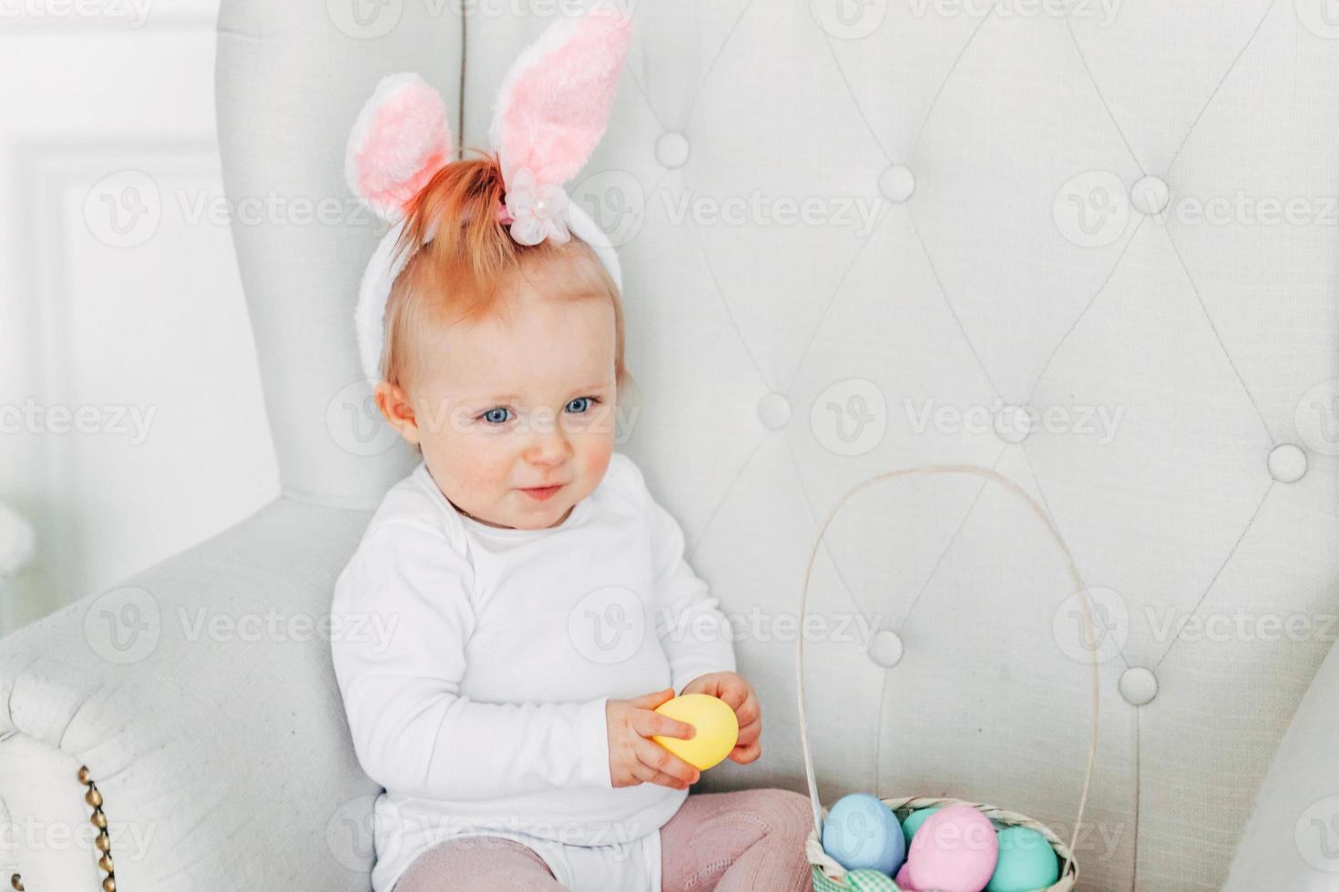 Little child girl wearing bunny ears on Easter day and playing with painted eggs photo