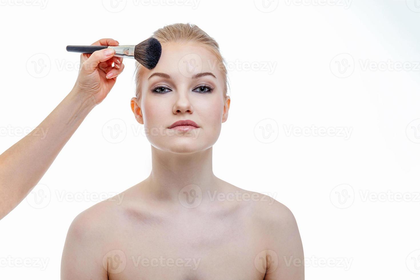 Hand of makeup master applying powder for young woman model on white background. Professional make up applying by artist. Beautiful girl face with perfect skin. Make-up detail in process. photo