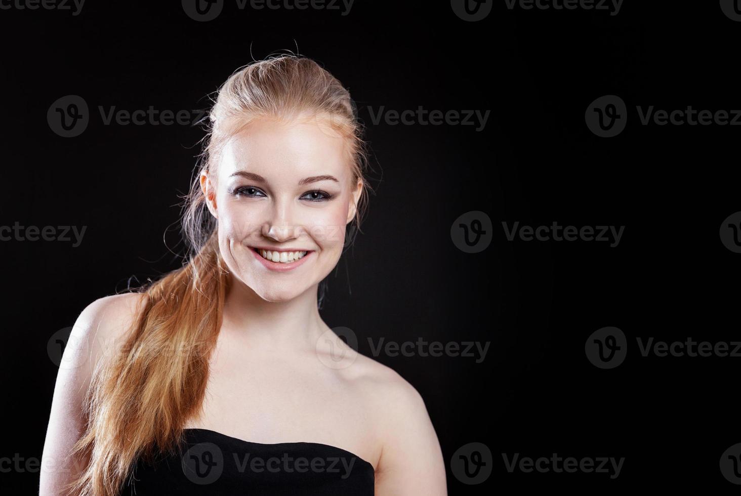 Beauty fashion model girl with long healthy smooth straight hair ponytail hairstyle on black background. Smiling pretty woman looking camera. Perfect Fresh Skin Portrait. Youth and Skin Care Concept. photo