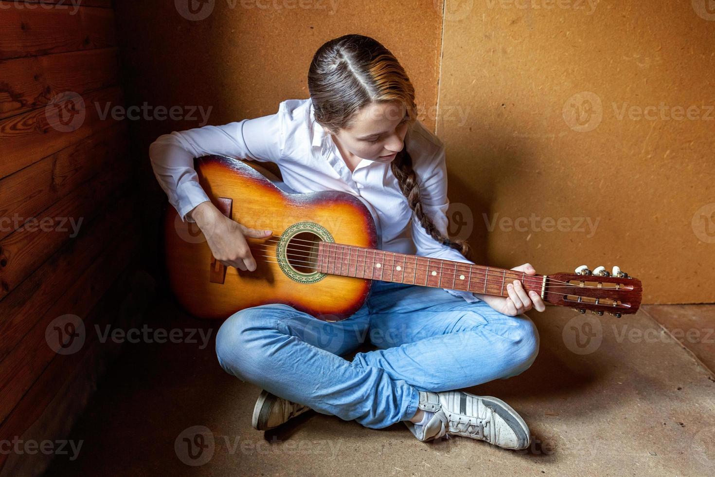 Young hipster woman sitting on floor and playing guitar at home. Teen girl learning to play song and writing music in her room. Hobby, lifestyle, relax, Instrument, leisure, education concept. photo