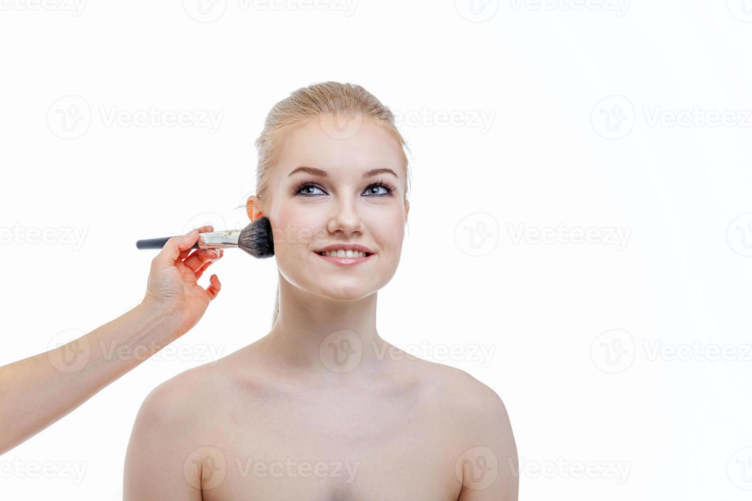 Hand of makeup master applying powder for young woman model on white background. Professional make up applying by artist. Beautiful girl face with perfect skin. Make-up detail in process. photo