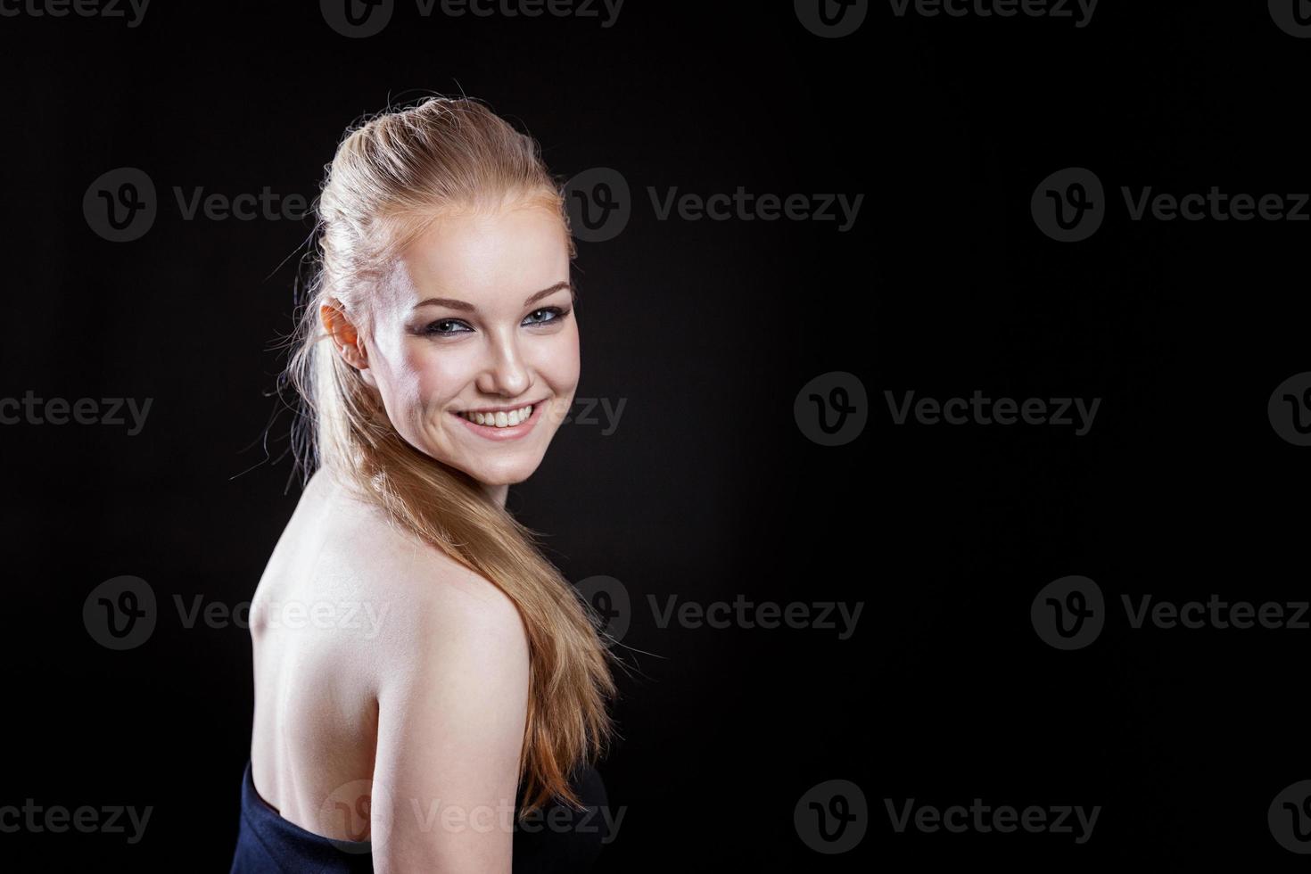 Beauty fashion model girl with long healthy smooth straight hair ponytail hairstyle on black background. Smiling pretty woman looking camera. Perfect Fresh Skin Portrait. Youth and Skin Care Concept. photo