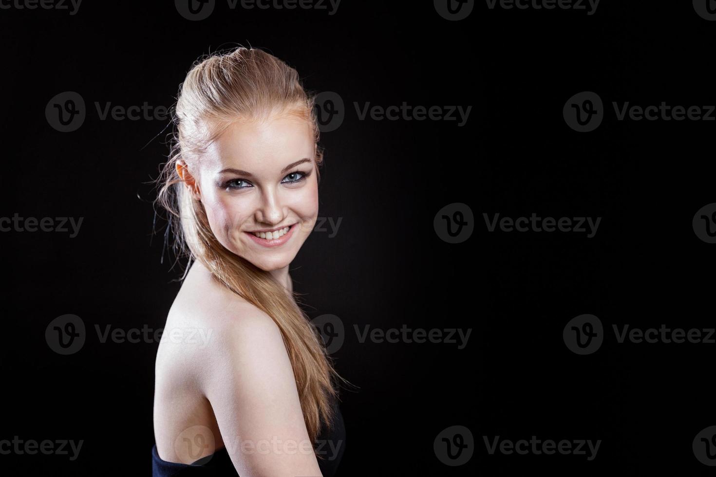 Beauty fashion model girl with long healthy smooth straight hair ponytail hairstyle on black background. Smiling pretty woman looking camera. Perfect Fresh Skin Portrait. Youth and Skin Care Concept. photo