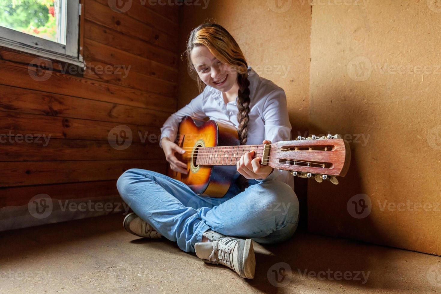 joven hipster sentada en el suelo y tocando la guitarra en casa. adolescente aprendiendo a tocar canciones y escribiendo música en su habitación. hobby, estilo de vida, relajación, instrumento, ocio, concepto de educación. foto