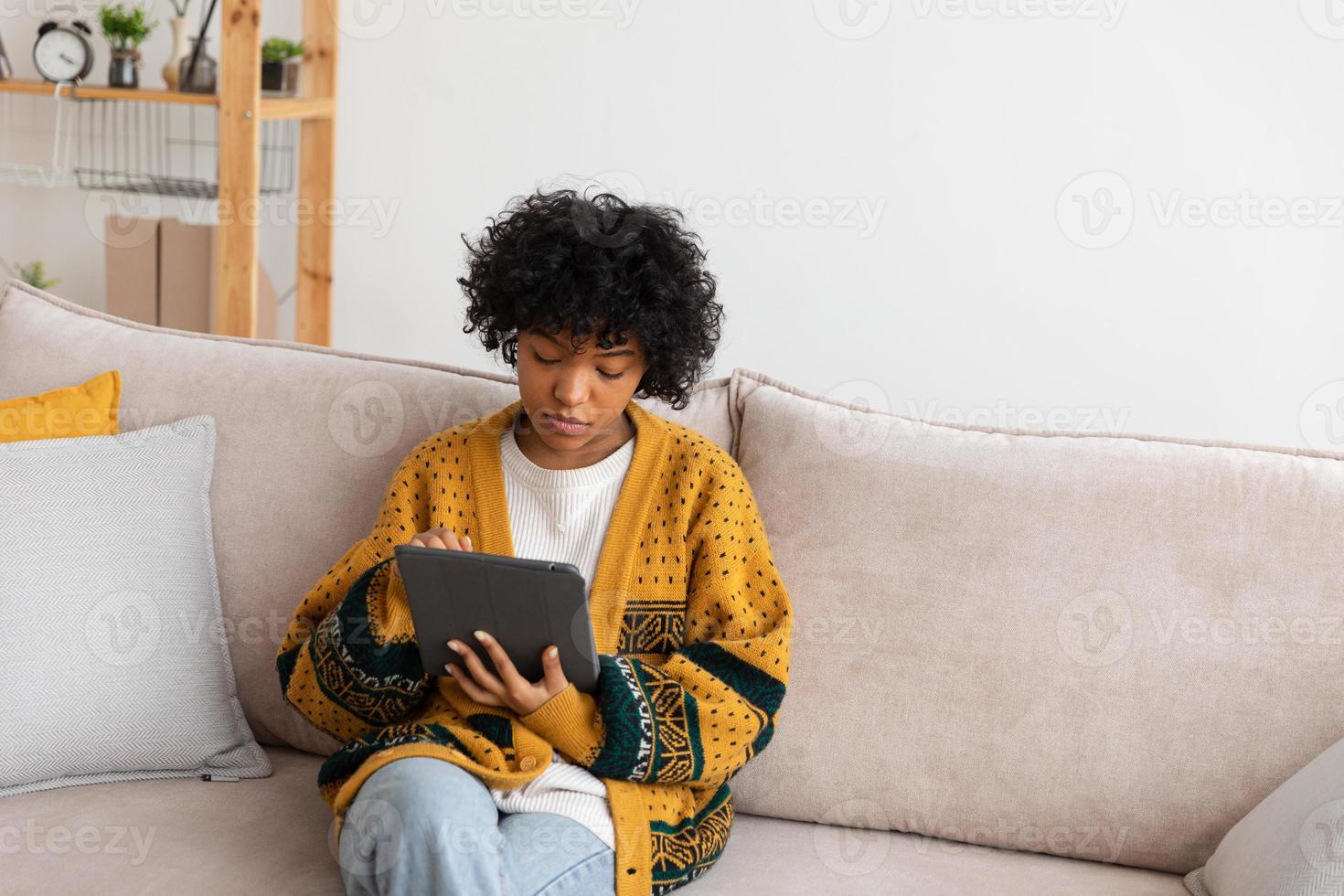 African american girl holding digital tablet touch screen typing scroll page at home. Woman with mobile tech device surfing internet using social media apps playing game. Study work shopping online. photo