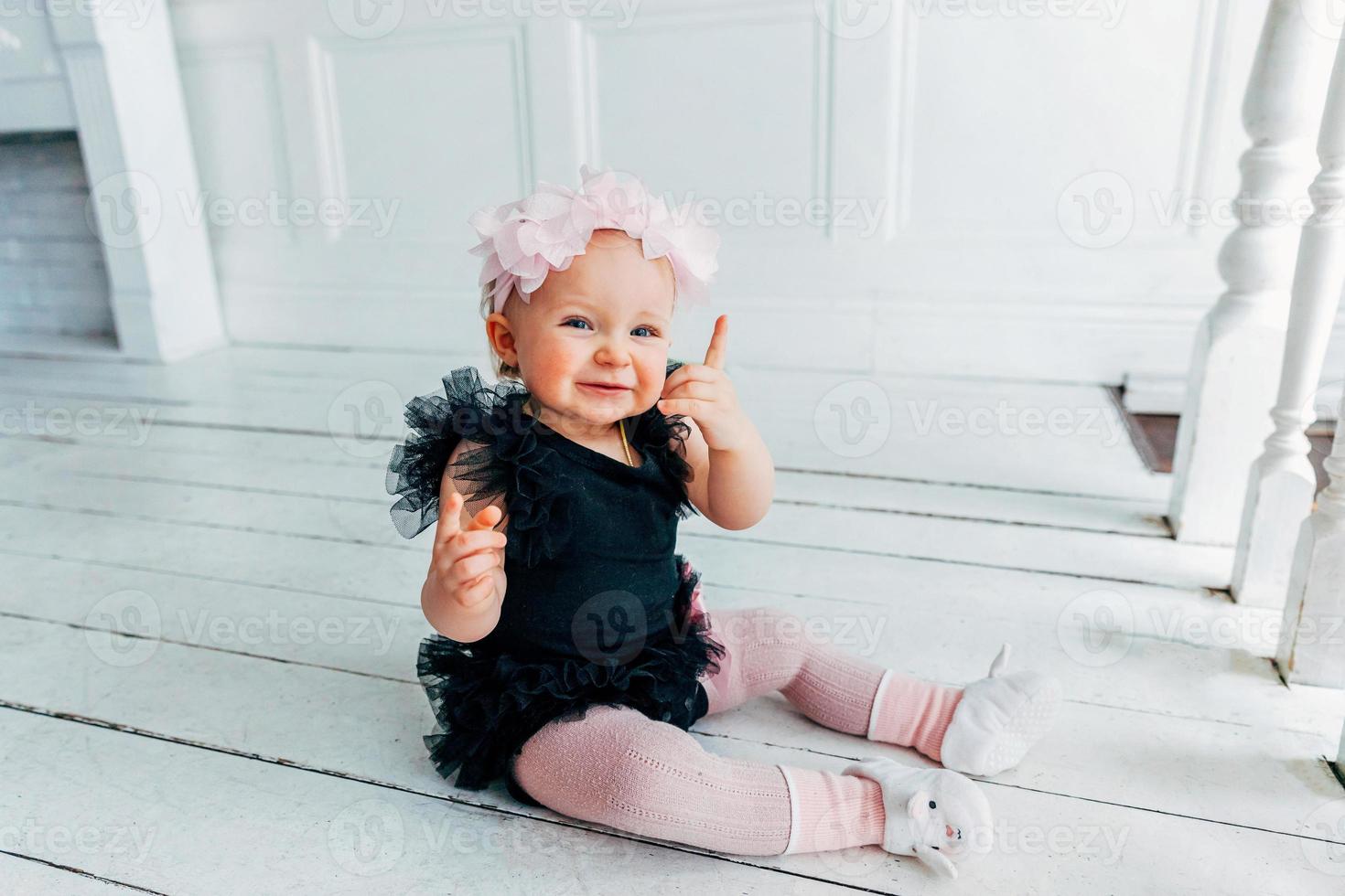 Little crawling baby girl one year old siting on floor in bright light living room smiling and laughing photo