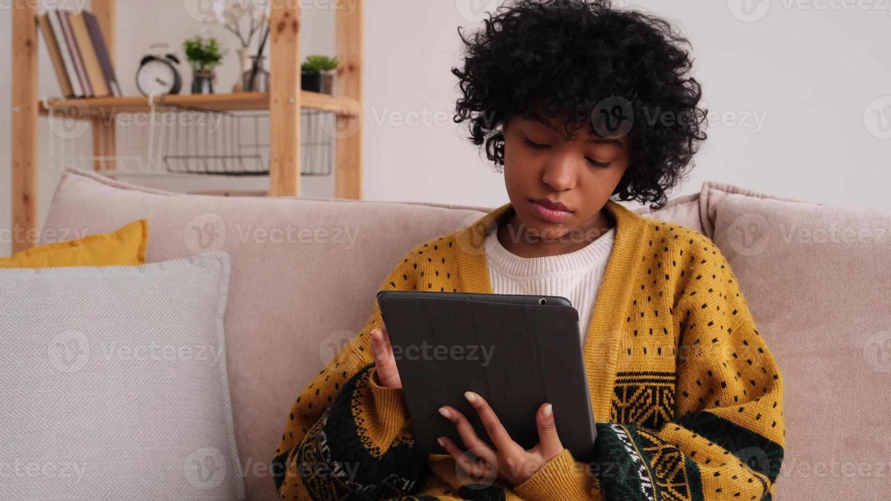 African american girl holding digital tablet touch screen typing scroll page at home. Woman with mobile tech device surfing internet using social media apps playing game. Study work shopping online. photo