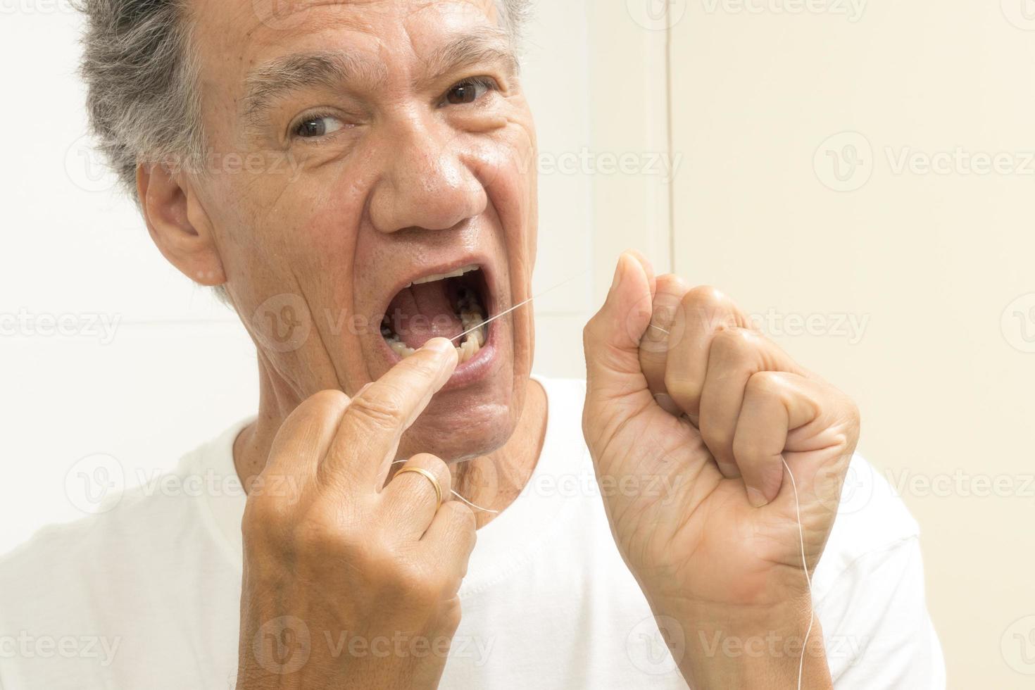 Senior man flossing his teeth with dental floss photo