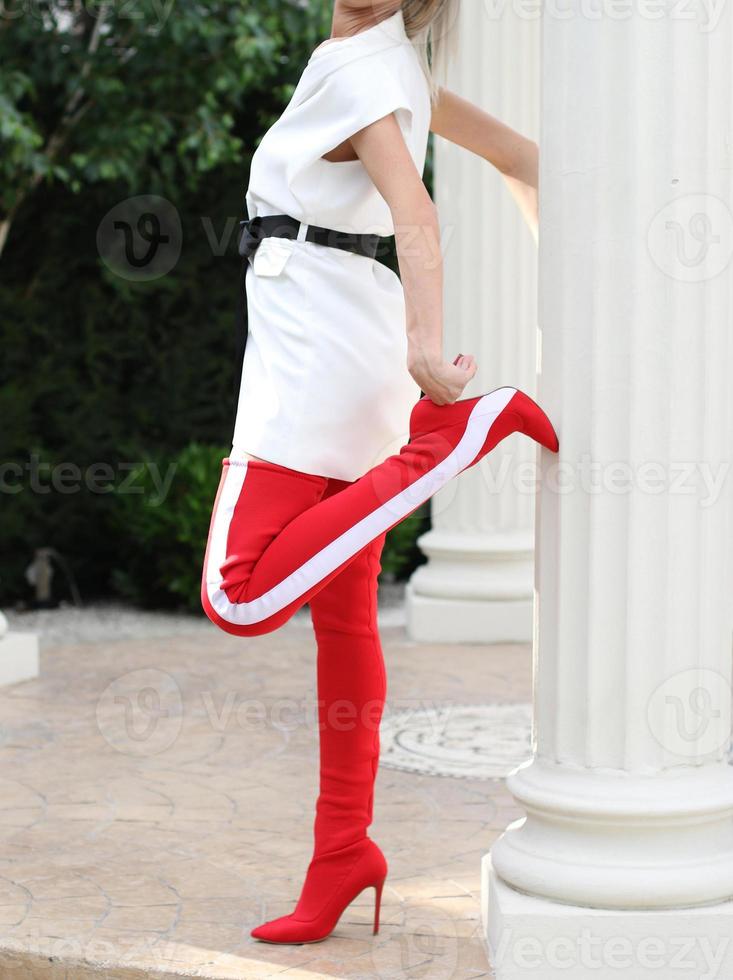 modelo con un vestido blanco y botas altas de cuero rojo está tomando una foto