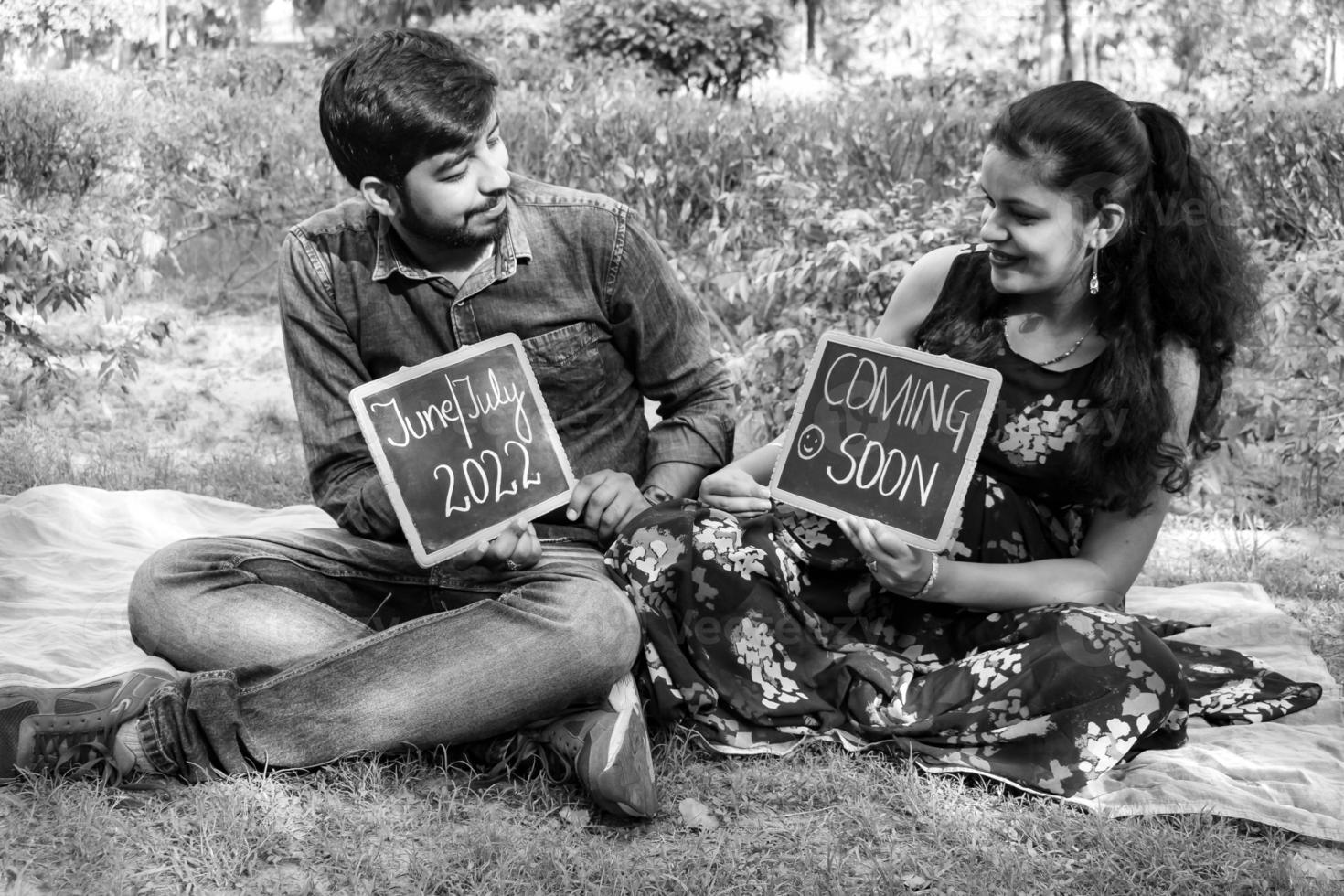 Indian couple posing for maternity baby shoot. The couple is posing in a lawn with green grass and the woman is falunting her baby bump in Lodhi Garden in New Delhi, India photo