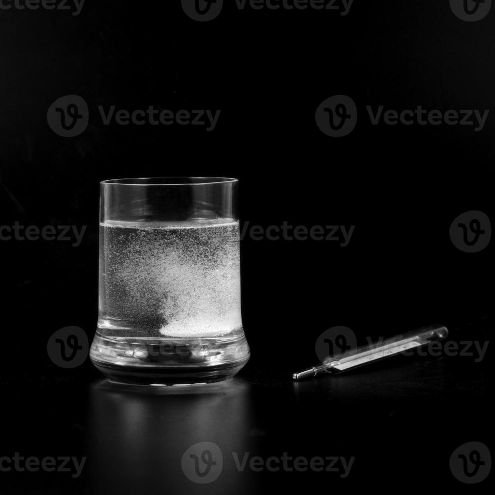 An effervescent tablet in the glass with a thermometer beside it to measure the fever photo