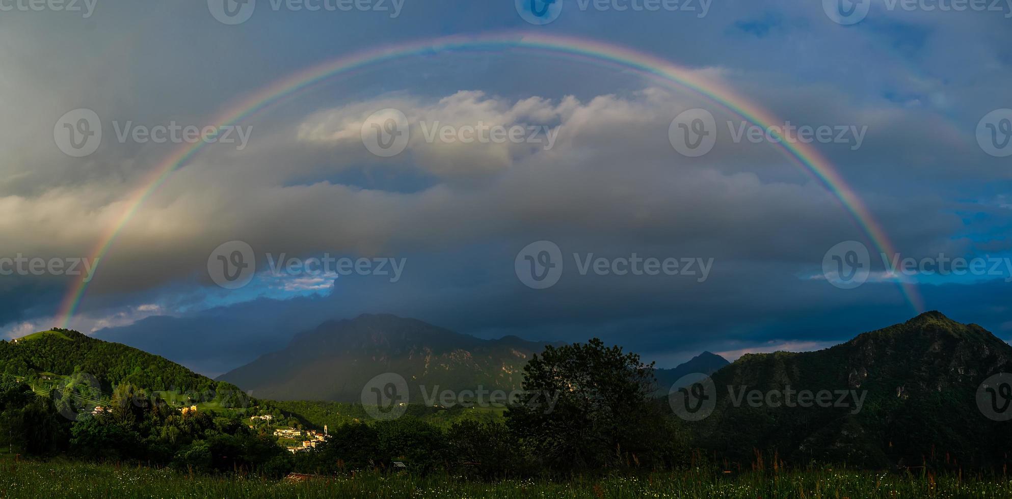 arco iris real sobre un pequeño pueblo en las montañas al atardecer foto