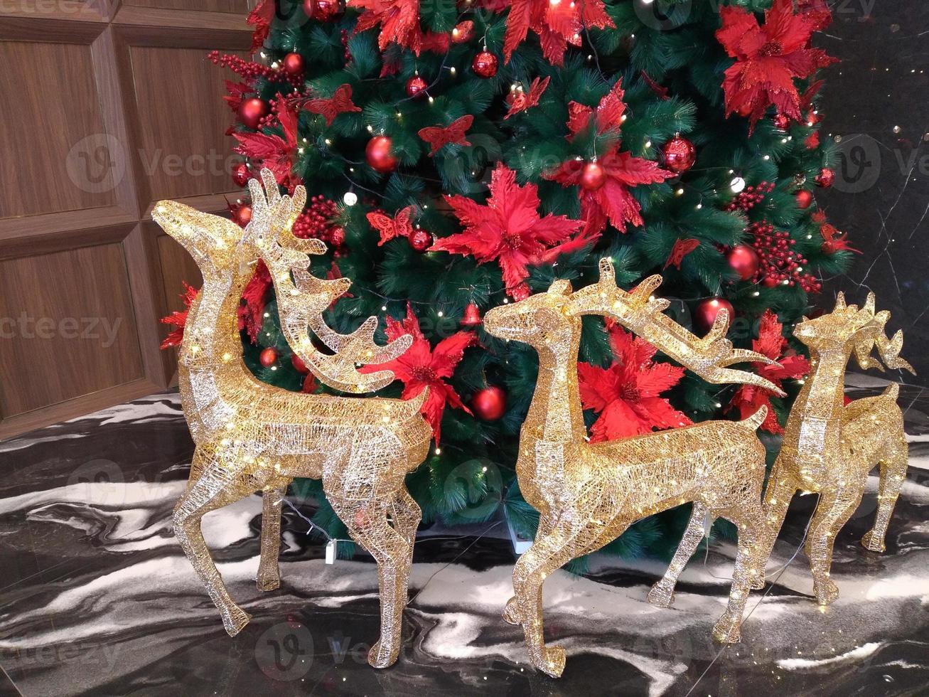 The Christmas tree is decorated with red balls and red ribbons with golden deer around it which looks beautiful, perfect for a Christmas background. photo