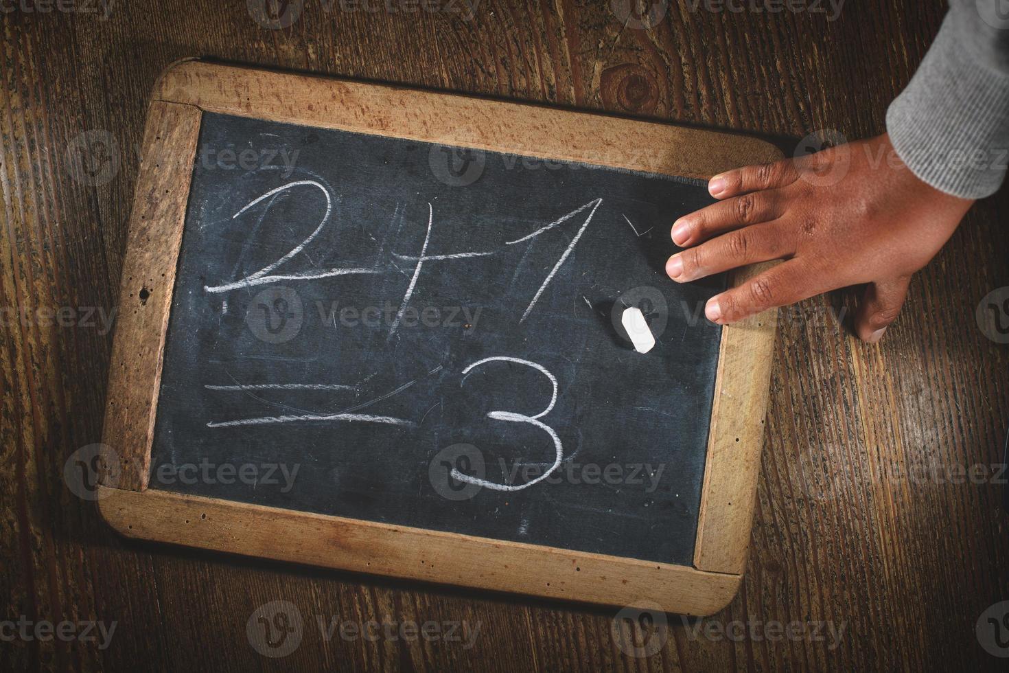 Child hand after writing simple math calculation on small blackboard with chalk photo