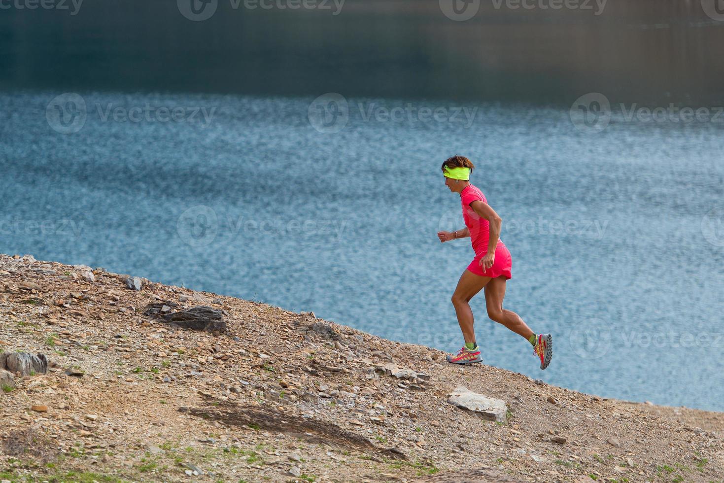 Woman gets workout running trail near an alpine lake photo