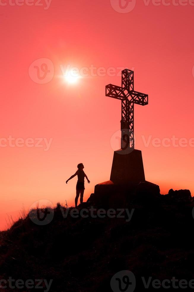 cruz en la cima de una montaña con mujer de brazos abiertos foto