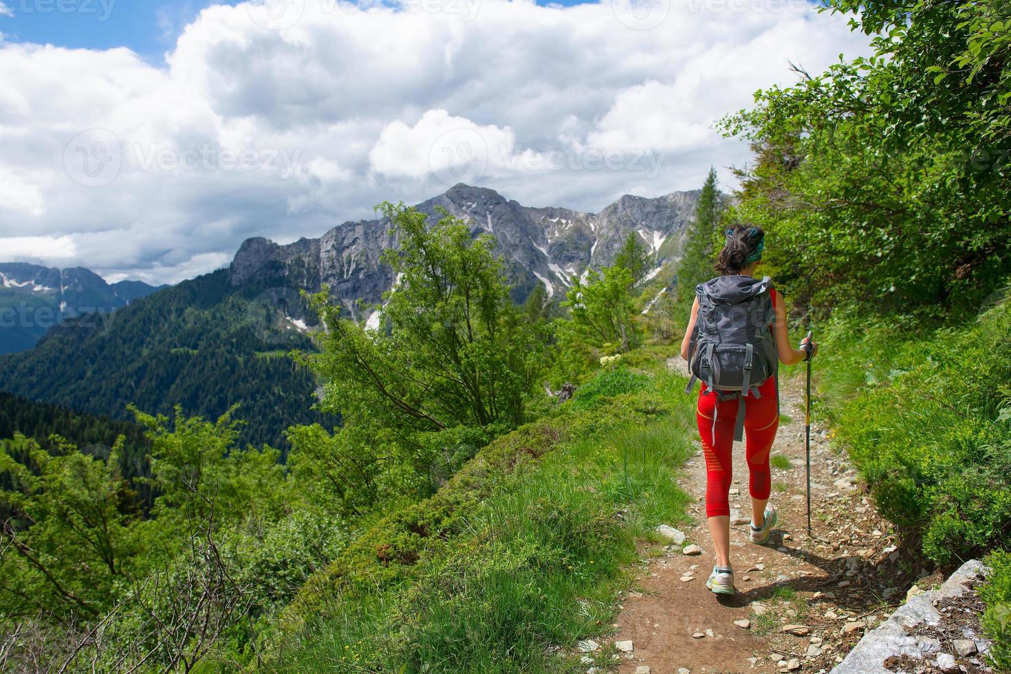 chica con mochila y bastones durante un trekking alpino sola foto