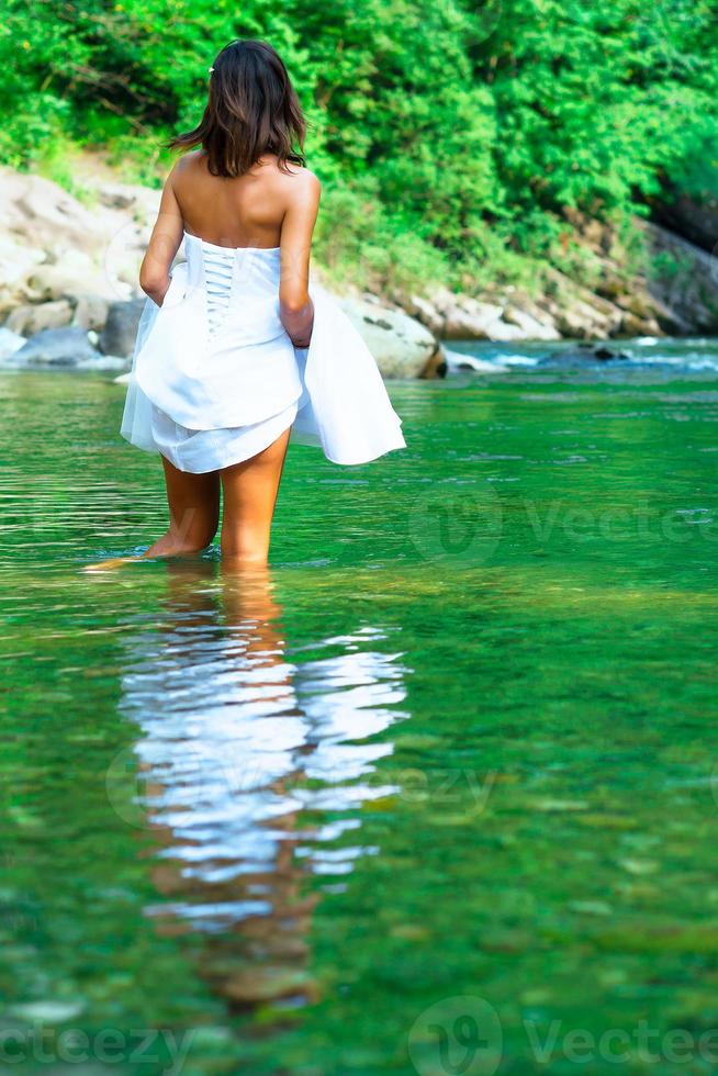 Young, beautiful and lonely bride It gets wet legs in a river. photo