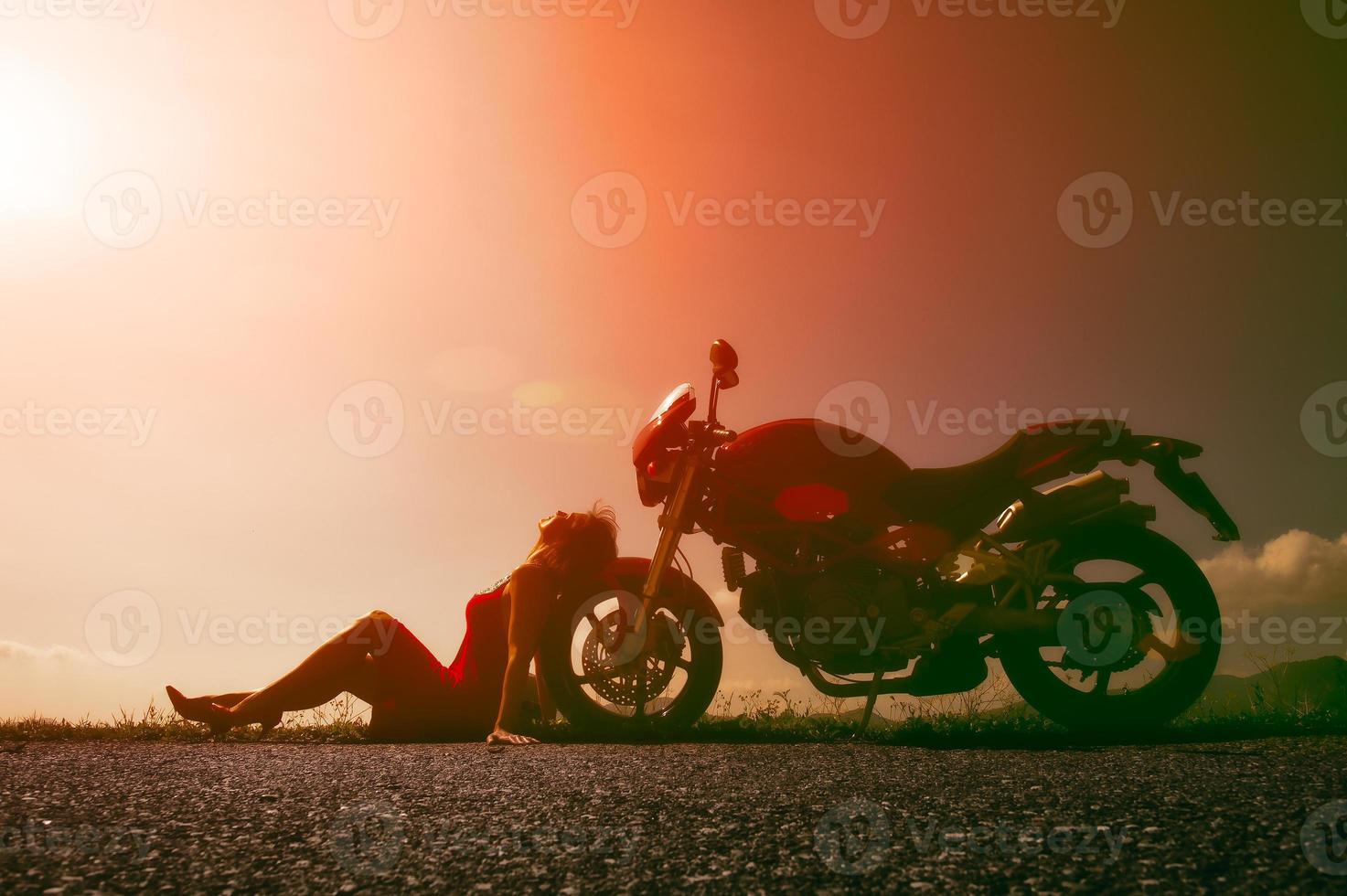 Girl resting in the sun sun leaning against the wheel of his motorcycle photo