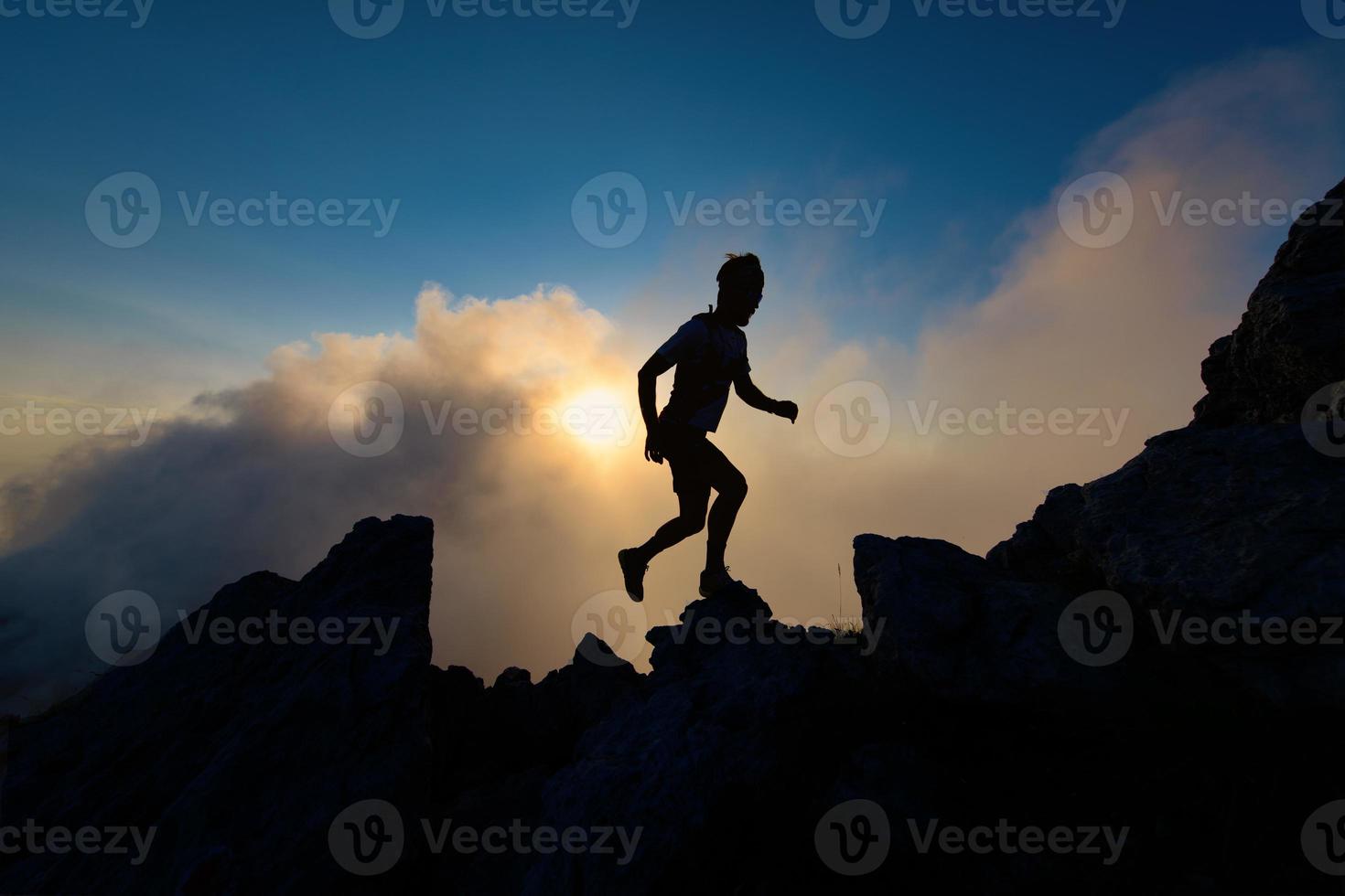 Silhouette of man on rocky ridge in mountain running uphill photo