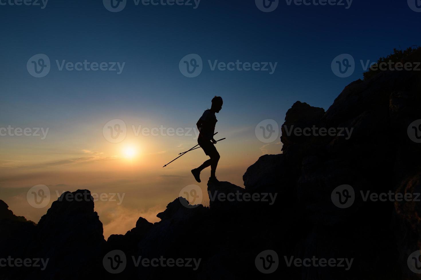 silueta al atardecer del hombre skyrunner escalando la cresta alpina con bastones foto