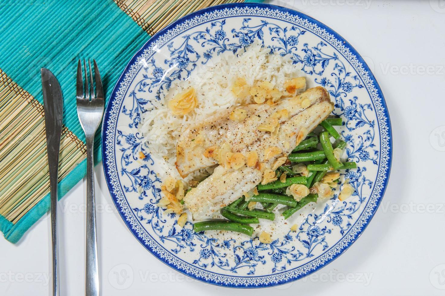 pescado frito al estilo libanés en un plato para servir con arroz con sabor a cebolla y rodajas de almendras tostadas. foto