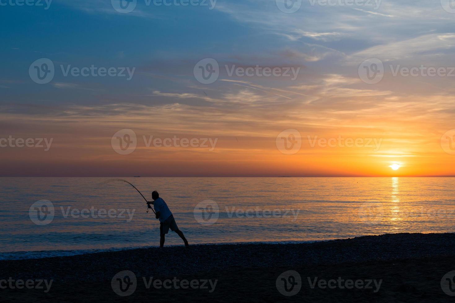 pescador con caña de pescar hace el lanzamiento en el mar foto