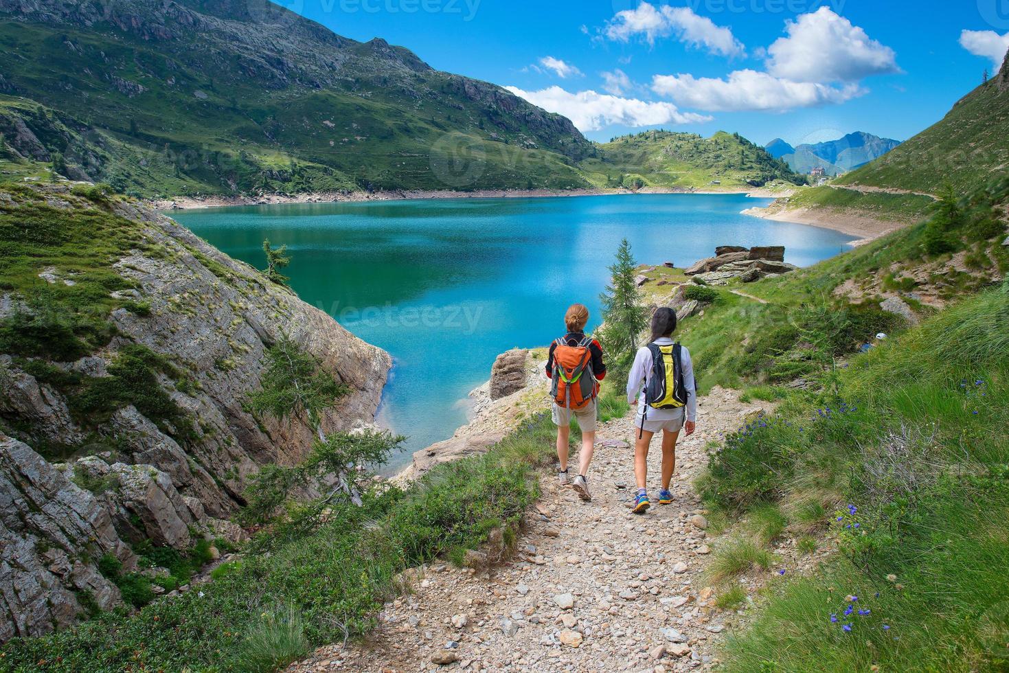 Two friends during a hike in the mountains walking near an alpin photo