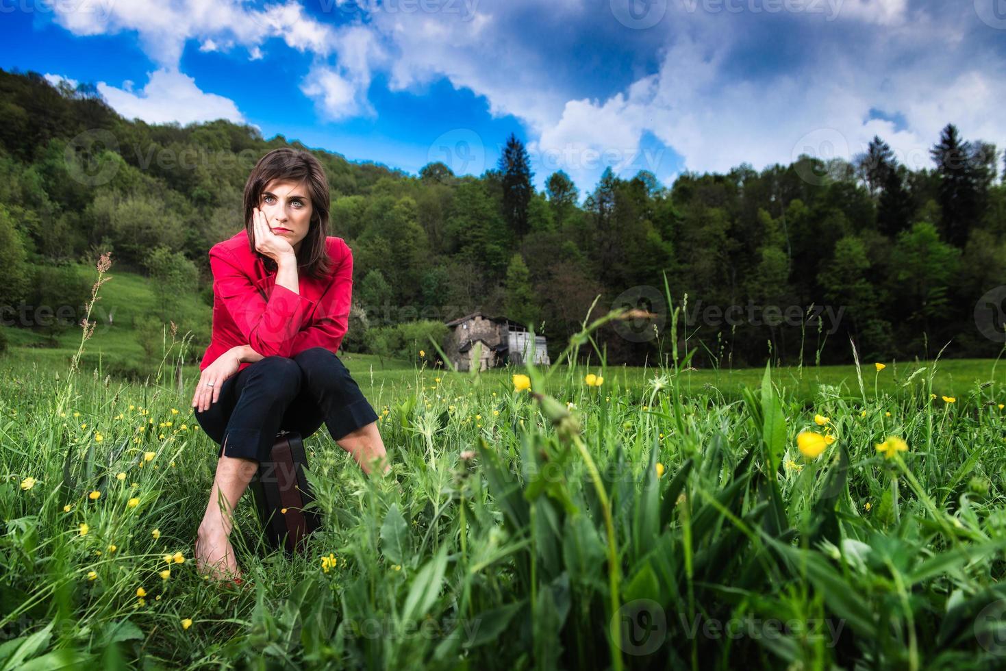 mujer elegante sentada en una maleta en medio de un prado foto