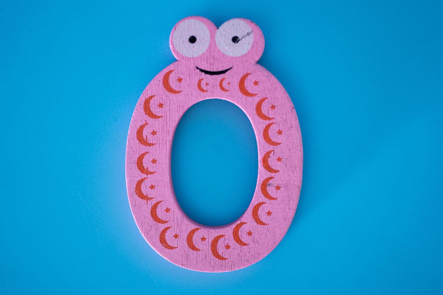 Cute and colorful wooden numeral 0 with eyes on a blue background. photo