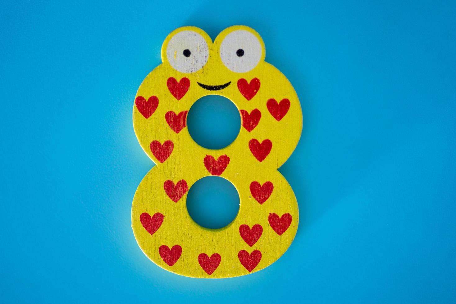 Cute and colorful wooden number 8 in yellow with eyes on a blue background. photo