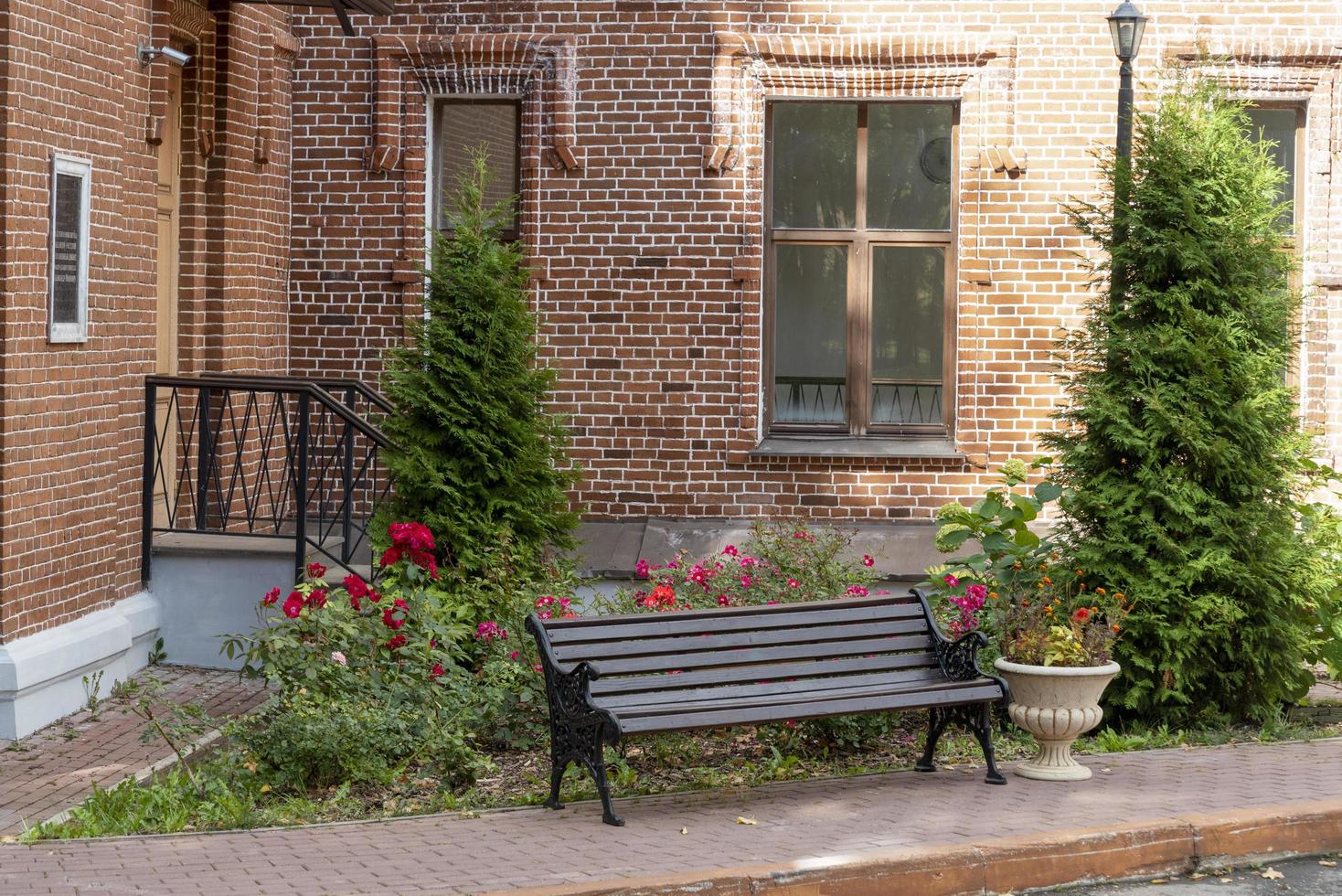 Wooden bench on the background of a brick house with flowers and trees. photo