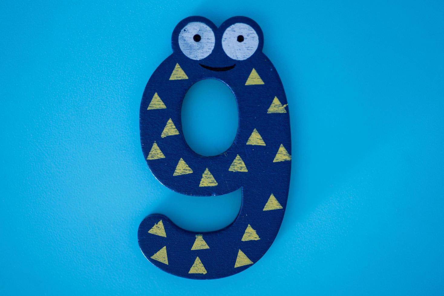 Cute and colorful wooden number 9 in blue with eyes on a blue background. photo