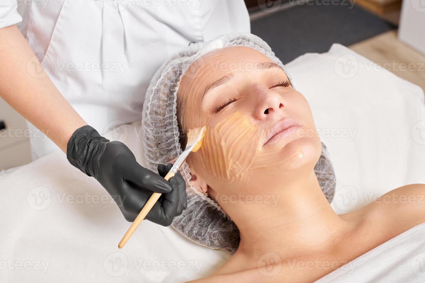 cosmetóloga aplica máscara de miel en la cara de la mujer para hidratar la piel de la cara en el salón de belleza spa foto