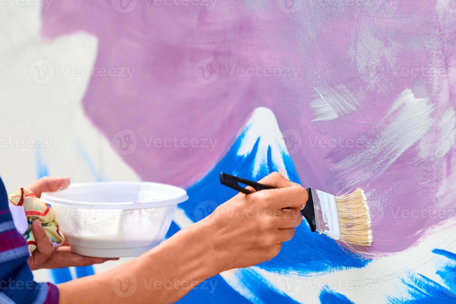 Female artist working on abstract acrylic painting, hand moving paint brush, large canvas outdoor photo