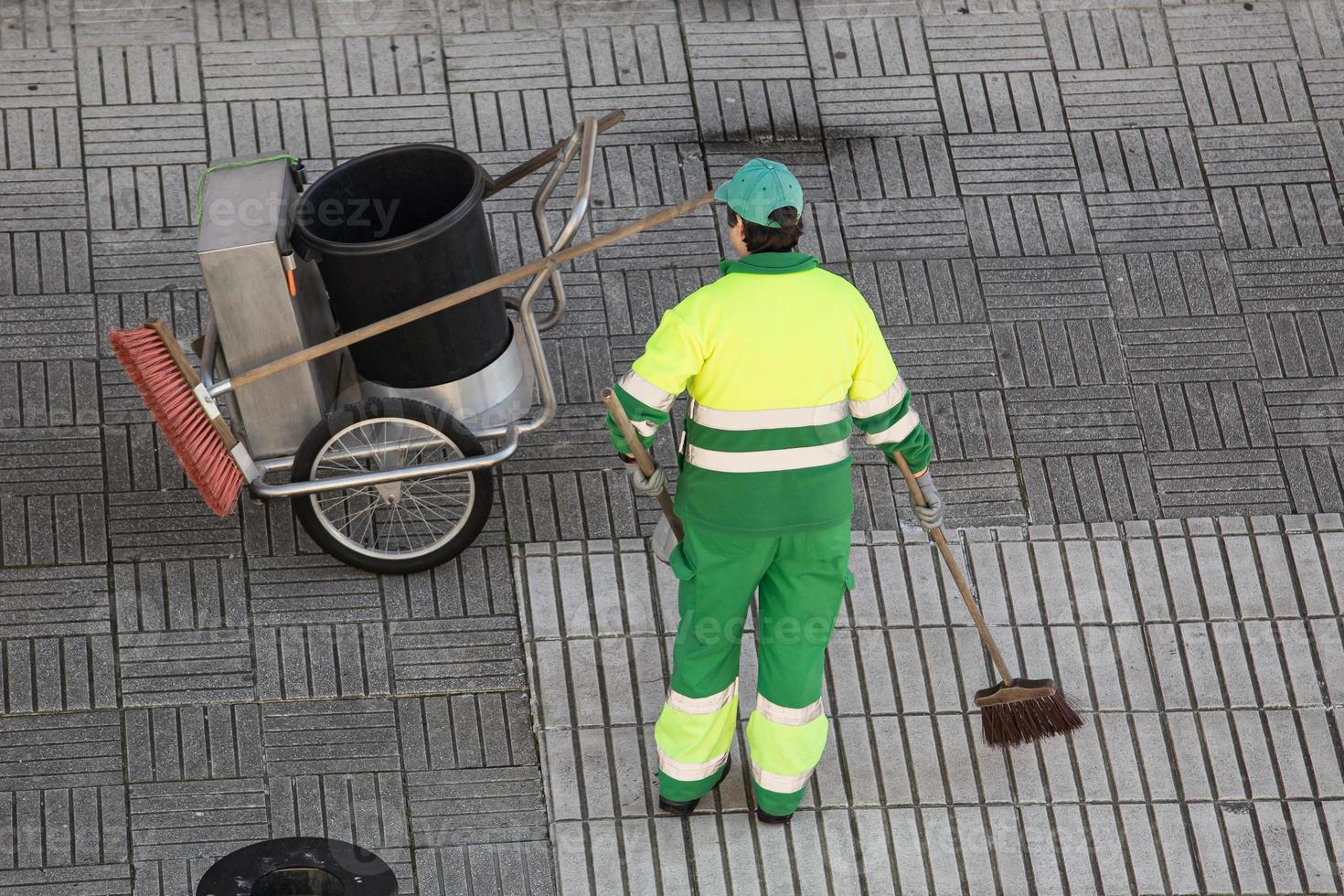 Street sweeper working on a sidewalk with her shovel, trolley and broom photo