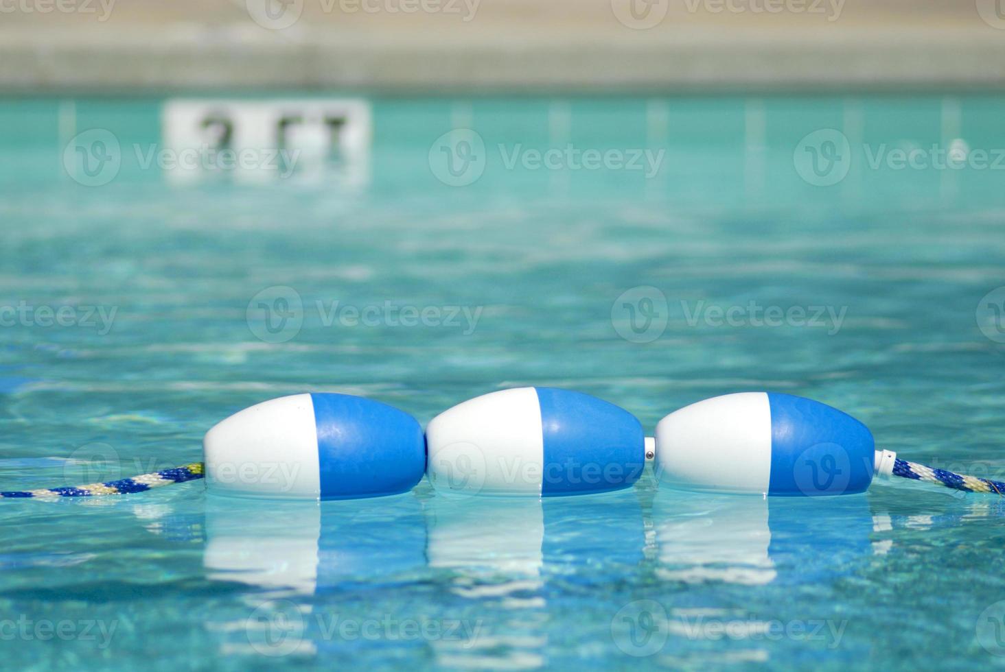 Three bouys in a crystal clear blue swimming pool with a sign marked 3 ft in the background. photo