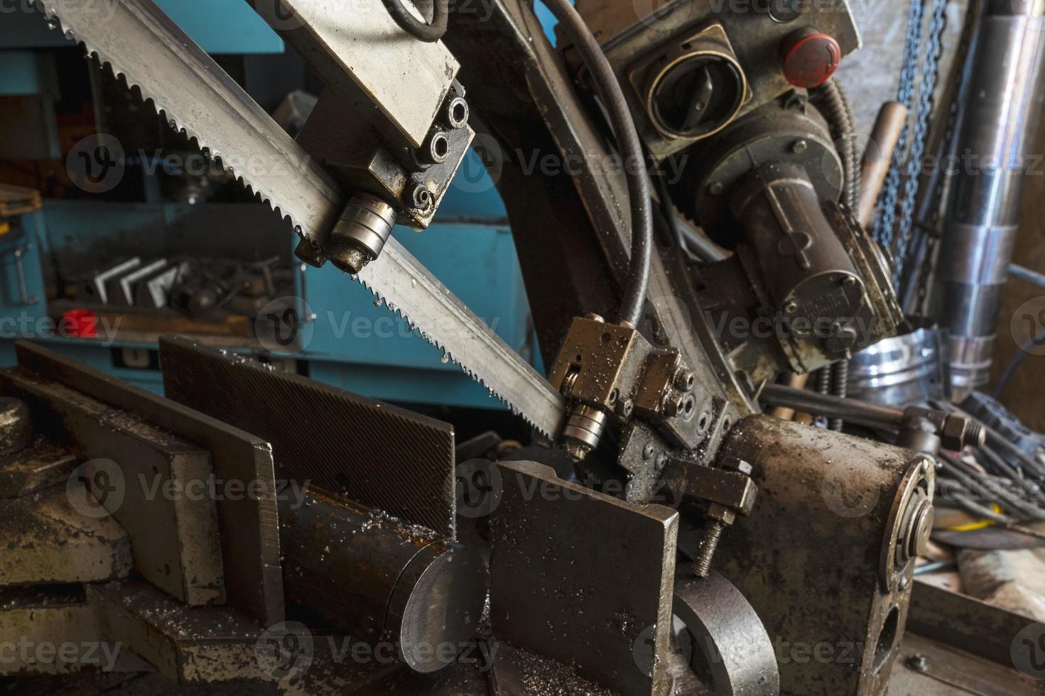 A metal band saw in the workshop cuts a metal rod with a liquid refrigerant. Gear blade of the machine photo
