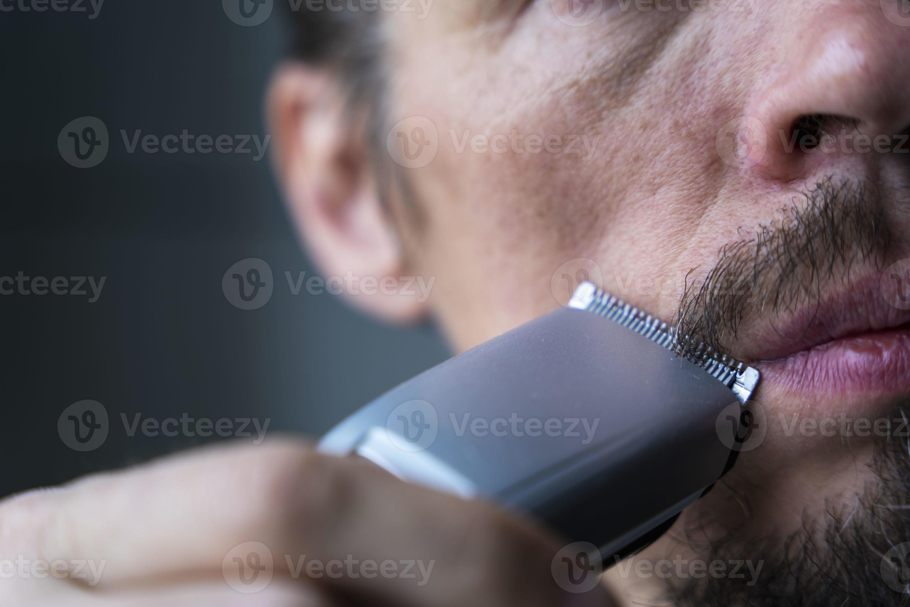 a man cuts his beard and mustache with an electric razor, time to shave