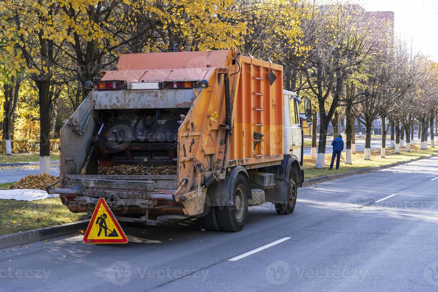 camión de basura elimina las hojas caídas de otoño, eliminación de hojas de otoño caídas por parte de los empleados de servicios públicos foto